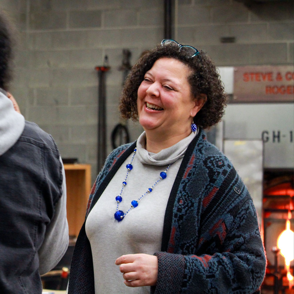 Color photograph of Dr. Kimberly Keith laughing and talking to a student in the Hilltop Heritage Middle School hot shop.