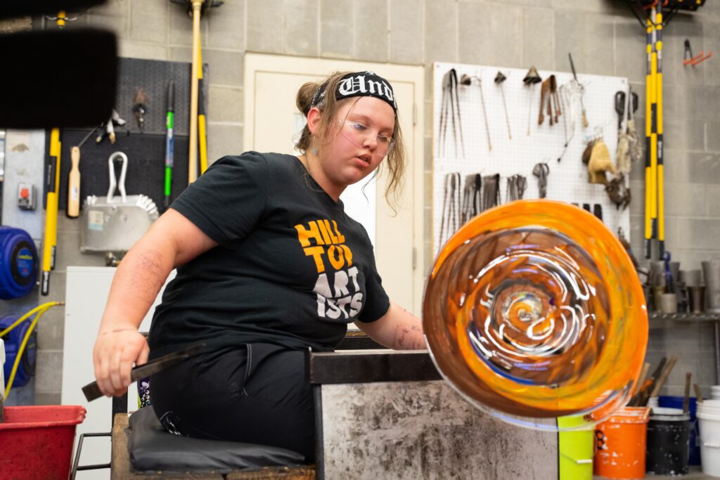 Hilltop Artists student, Dasein, makes a glass plate in the hot shop at Hilltop Heritage, October 2022.