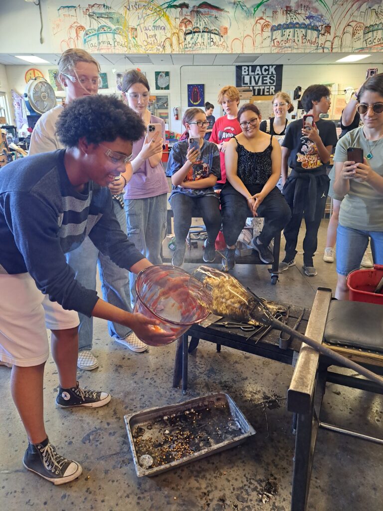 Students in the summer program at Hilltop Artists popping popcorn during a demonstration in the hot shop, July 2023.